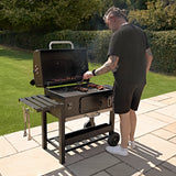XXL BBQ smoker grill with a sleek black finish, grilling meats outdoors on a stone patio, surrounded by lush greenery
