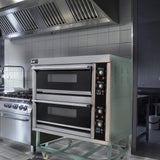 Large commercial KuKoo pizza oven with stainless steel finish, two black baking chambers, and control panel in a modern kitchen setting