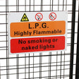 Metal mesh gas bottle cage with warning signs, featuring orange and red colors, designed for safety and secure storage of gas bottles