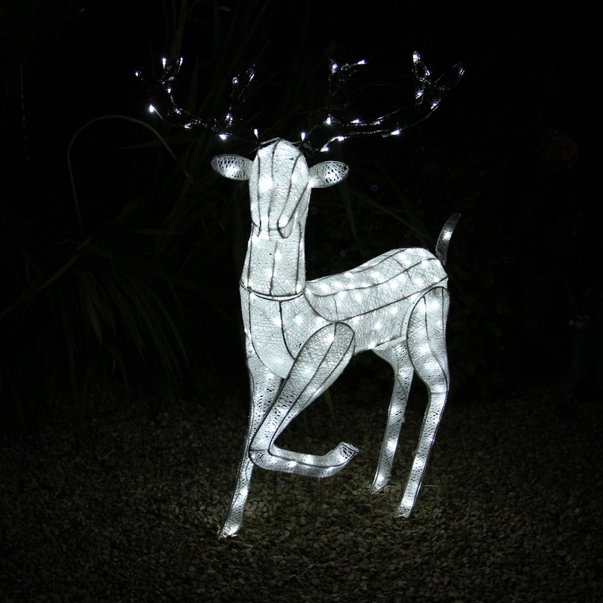 Glowing white reindeer with antlers, adorned with bright lights, standing on a gravel surface, perfect for festive outdoor decor