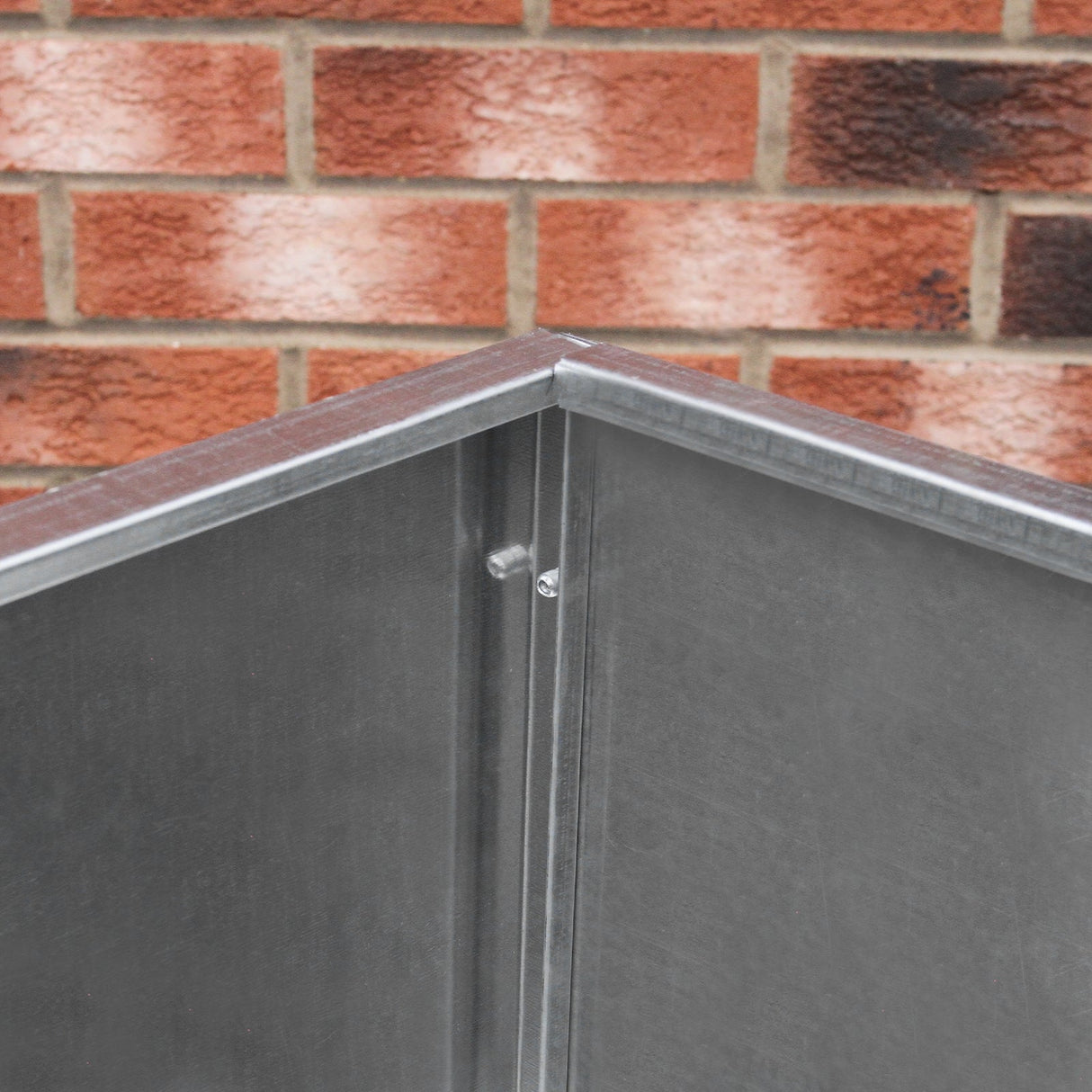 Galvanised feed store with a single compartment, featuring a sturdy metal construction and a sleek, shiny surface against a brick backdrop