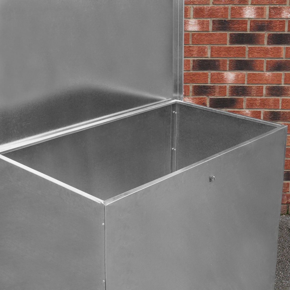Galvanised feed store with a single compartment, featuring a shiny metal finish and a spacious, open interior against a brick background