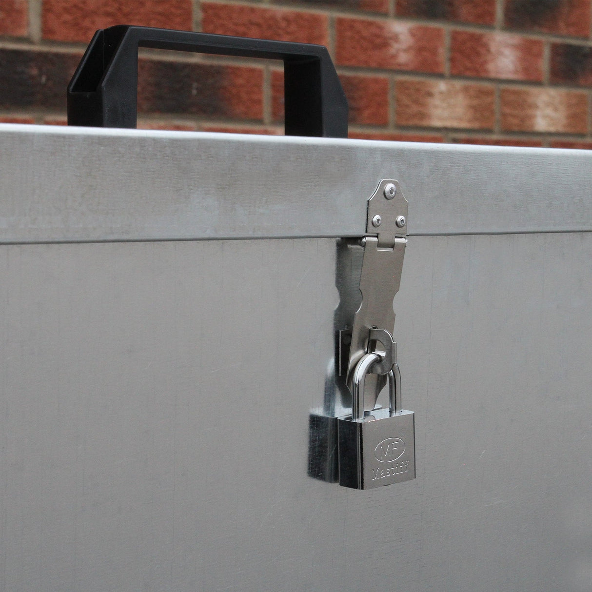 Galvanised feed store with three compartments, featuring a sturdy metal latch and a padlock for secure storage, against a brick background