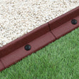 Flexible terracotta lawn edging, 1.2m long, featuring a textured surface and black connectors, separating gravel and grass areas