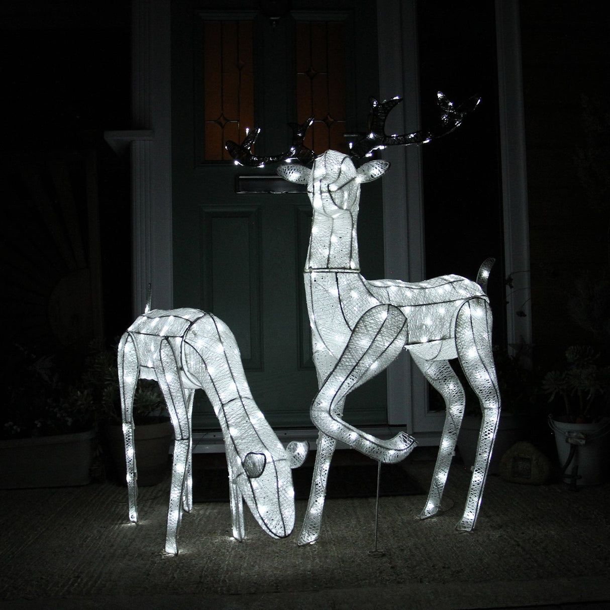Large light-up stag and doe reindeer set with a shimmering white wire frame, featuring intricate details and glowing accents, perfect for festive decor
