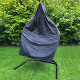 Grey hanging rattan egg chair covered with a protective tarp, set against a lush green hedge on a grassy area