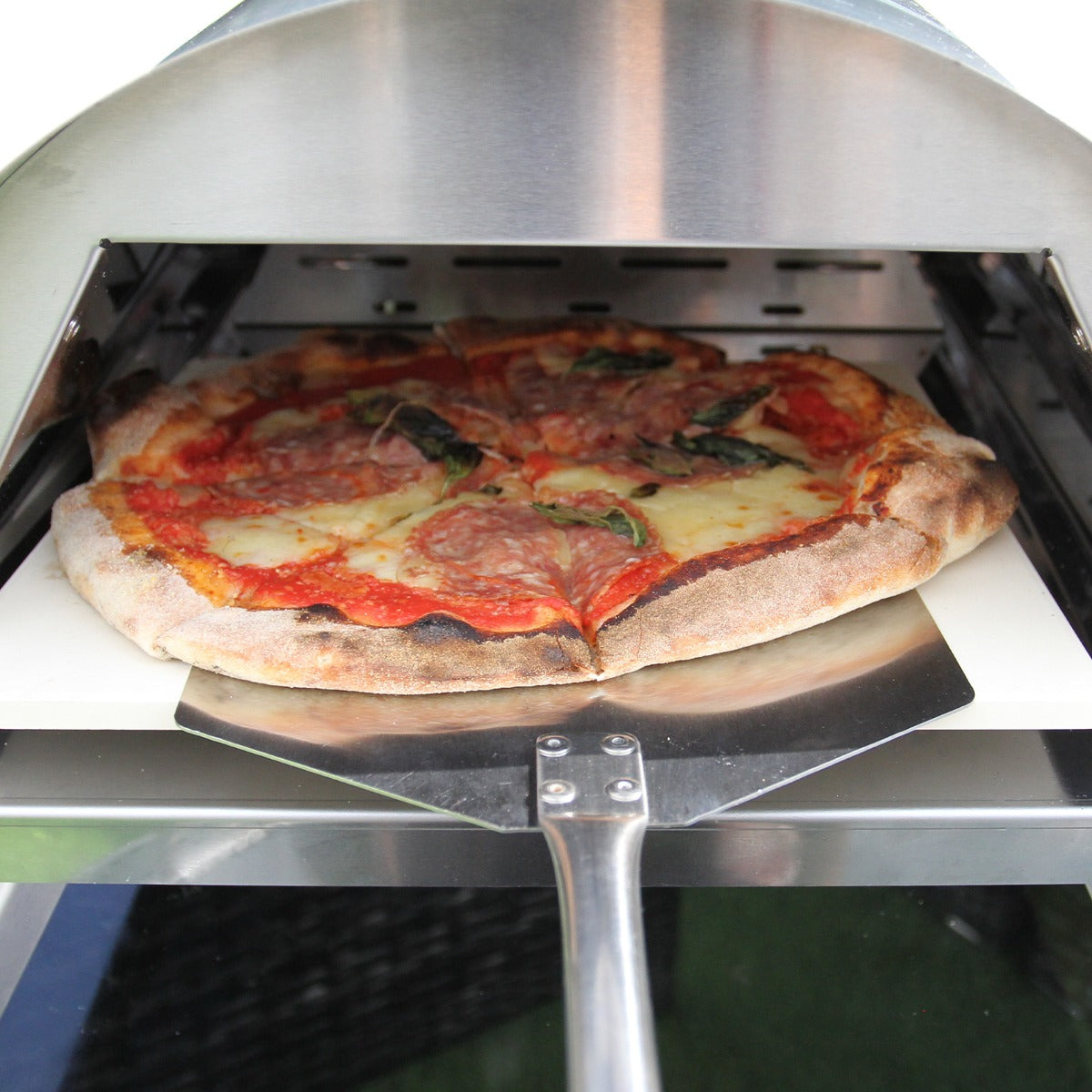 Freshly baked pizza with pepperoni and basil, resting on a stone inside a sleek outdoor pizza oven with stainless steel finish