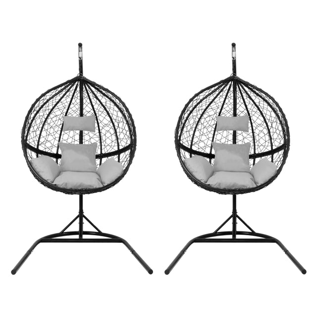 Two black hanging rattan egg chairs with plush white cushions, featuring a circular woven design and sturdy metal stands