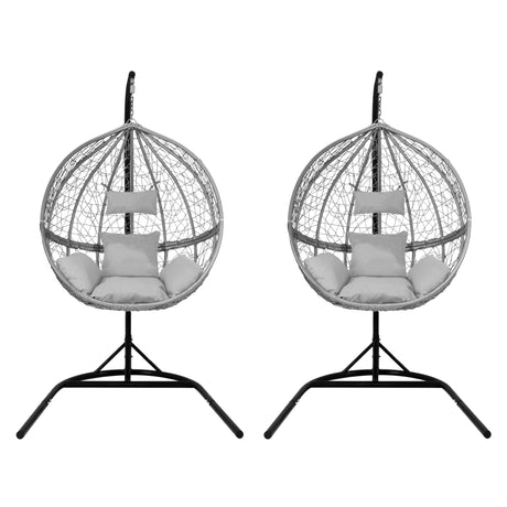 Two grey hanging rattan egg chairs with plush cushions, featuring a sleek black metal stand and a woven, airy design