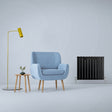 Matte black flat panel radiator beside a light blue armchair, yellow lamp, and wooden side table with a small plant