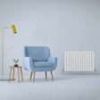 Gloss white designer flat panel radiator beside a light blue armchair and a small wooden side table with a plant, set against a soft gray wall