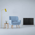 Sleek matt black flat panel radiator beside a light blue armchair and modern lamp, enhancing contemporary interior decor