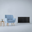 Matt black designer flat panel radiator with sleek vertical slats, positioned beside a light blue armchair and wooden side table