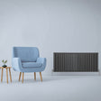 Anthracite grey designer flat panel radiator with sleek vertical slats, positioned beside a modern blue armchair and wooden side table