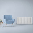 Gloss white flat panel radiator, 600mm x 1400mm, sleek design with vertical fins, positioned beside a modern blue armchair and wooden side table