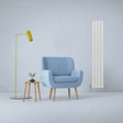 Gloss white designer flat panel radiator stands tall beside a blue armchair, yellow floor lamp, and wooden side table with a plant