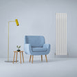 Gloss white designer flat panel radiator stands tall beside a cozy blue armchair and stylish side tables in a modern setting