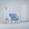Gloss white designer flat panel radiator standing tall beside a light blue armchair and modern floor lamp in a minimalist room