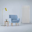 Gloss white designer flat panel radiator stands tall beside a blue armchair and a small wooden side table with a plant