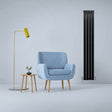 Sleek matt black flat panel radiator stands tall beside a light blue armchair and wooden side table with a small plant, enhancing modern decor