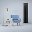 Sleek matt black flat panel radiator stands tall beside a light blue armchair and modern lamp, enhancing contemporary decor