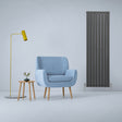 Anthracite grey designer flat panel radiator stands tall beside a blue armchair, yellow lamp, and small table with a plant