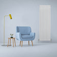 Gloss white designer flat panel radiator stands tall beside a blue armchair and modern lamp, enhancing a stylish interior space