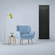 Sleek matt black flat panel radiator stands beside a light blue armchair and modern lamp, enhancing a stylish interior space
