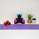 Colorful dumbbells on a purple exercise mat, with a black rack displaying weights and potted plants for a vibrant workout space
