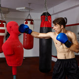 A muscular man in blue boxing gloves punches a large red free-standing boxing dummy in a gym with hanging punching bags