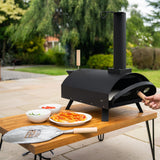 Classic outdoor pizza oven in sleek black, featuring a chimney, on a wooden table with fresh ingredients and a pizza peel nearby