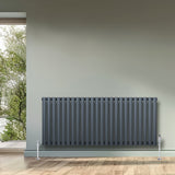 Anthracite grey oval single column radiator with sleek vertical bars, mounted on a light green wall, enhancing modern interiors