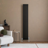 Sleek black oval single column radiator with chrome valves, mounted on a textured beige wall, enhancing modern interior decor