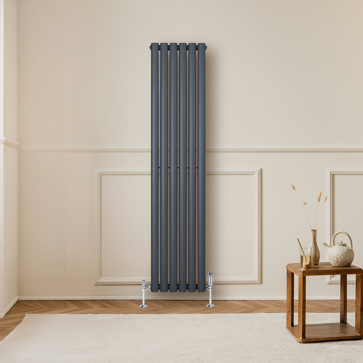 Sleek anthracite grey oval single column radiator mounted on a wall, complemented by stylish valves and a cozy room setting