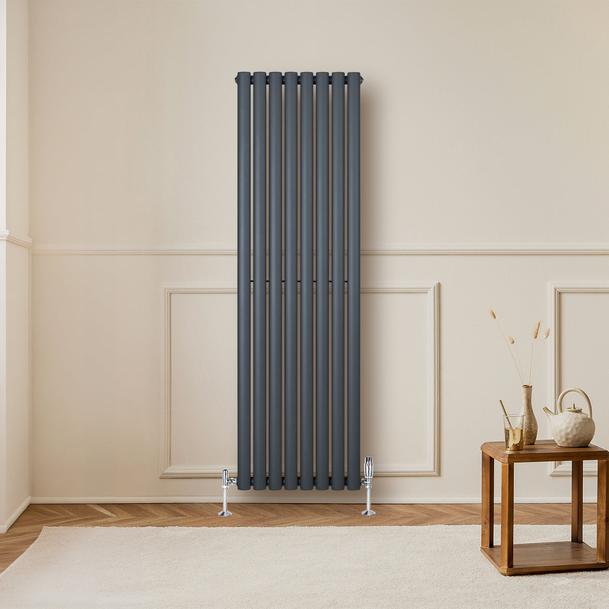 Sleek anthracite grey oval single column radiator mounted on a wall, complemented by stylish valves and a wooden table nearby