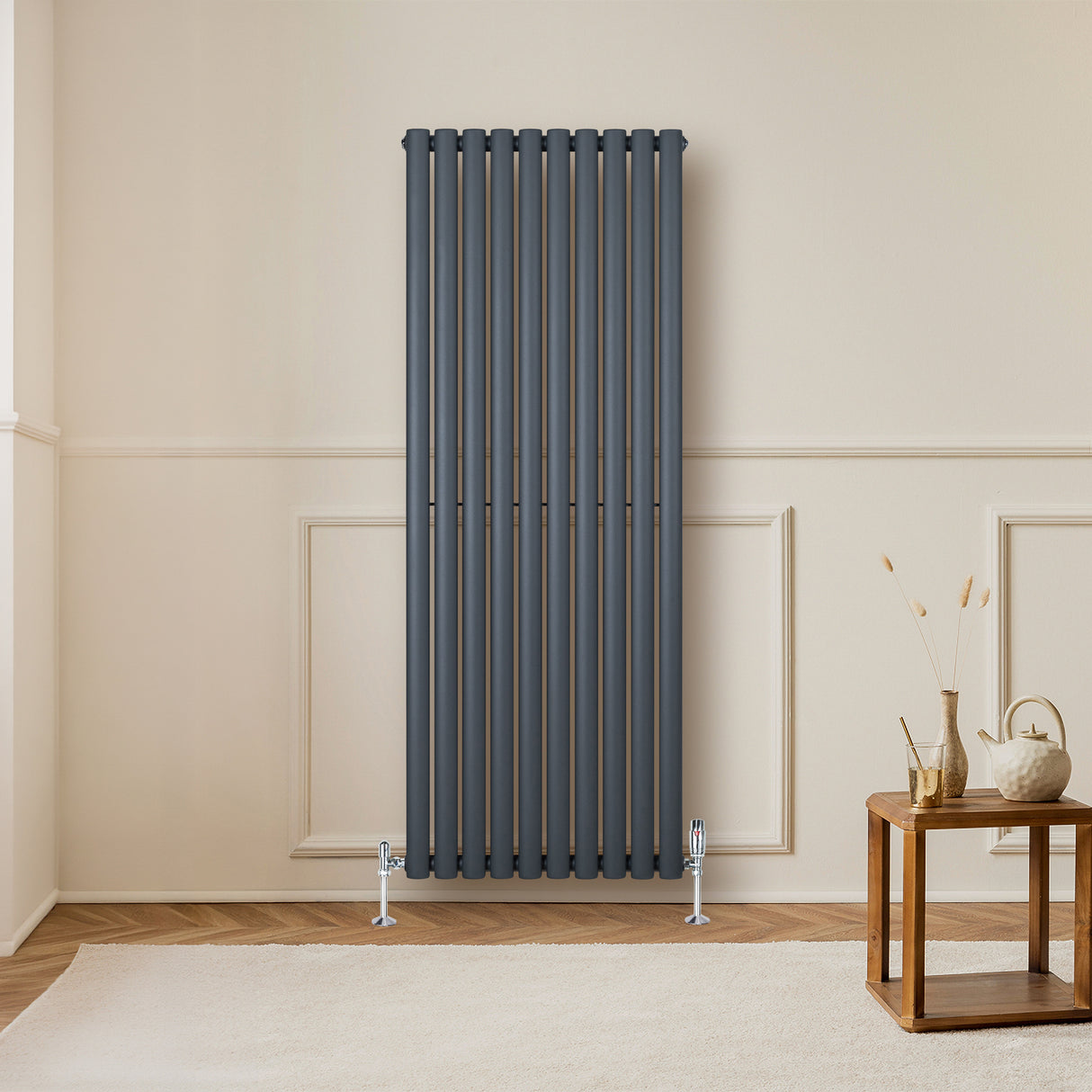 Sleek anthracite grey oval single column radiator mounted on a wall, complemented by stylish valves and a warm, inviting room setting