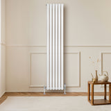 Sleek white oval single column radiator with five vertical panels, mounted on a light-colored wall, beside a wooden table