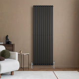 Sleek black oval single column radiator mounted on a textured beige wall, complemented by modern valves and a stylish living room setting