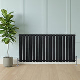 Sleek black flat single column radiator with polished valves, positioned beside a potted plant on a light wooden floor