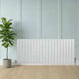 Sleek white flat single column radiator with vertical slats, mounted on chrome valves, beside a potted plant on a wooden floor