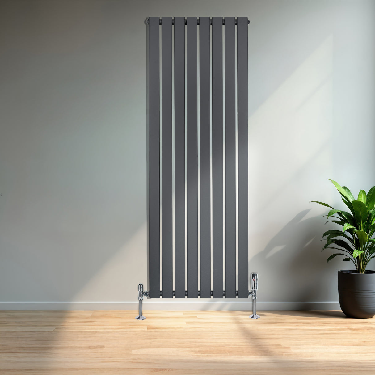 Sleek anthracite grey flat single column radiator with vertical slats, mounted on chrome feet, beside a potted plant in a modern room