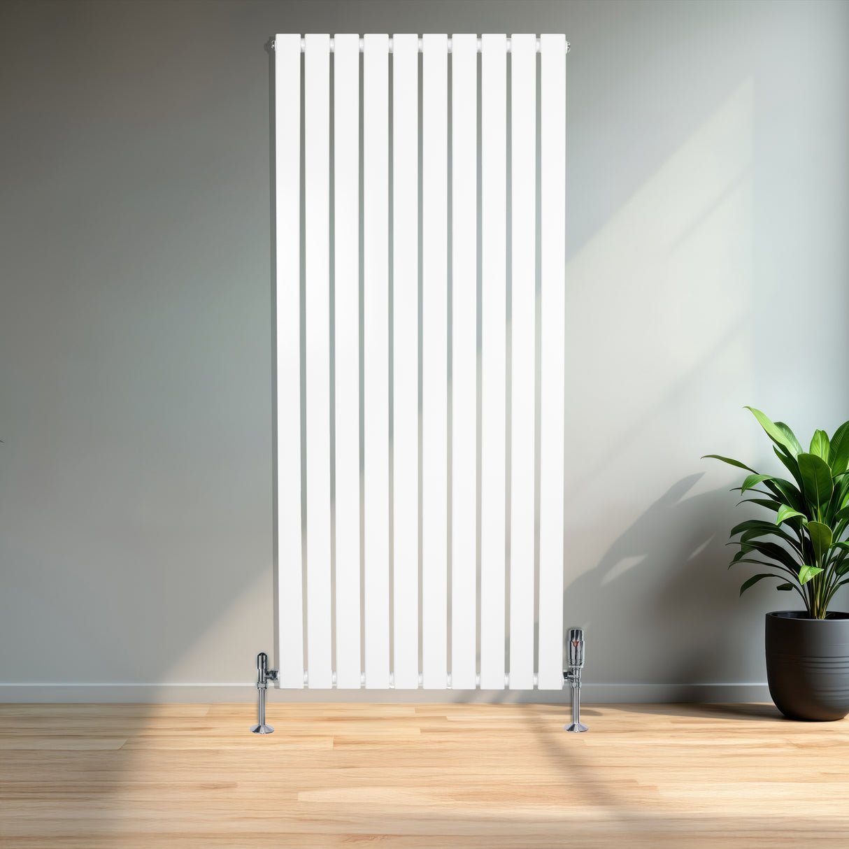Sleek white flat single column radiator with vertical slats, standing on chrome valves, set against a modern interior with wooden flooring and a potted plant