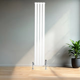 Sleek white flat single column radiator with chrome valves, standing tall against a modern interior backdrop with natural light