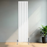 Tall, sleek white flat single column radiator with polished valves, set against a modern interior with wooden flooring and a green plant