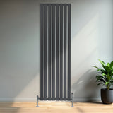 Tall anthracite grey flat single column radiator with vertical slats, mounted on chrome feet, set against a modern interior backdrop