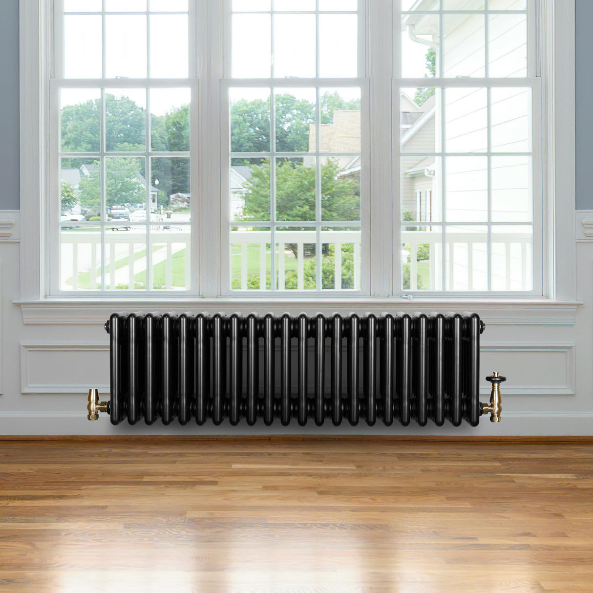 Traditional black 4 column radiator with brass valves, positioned under a large window, enhancing a warm, classic interior design
