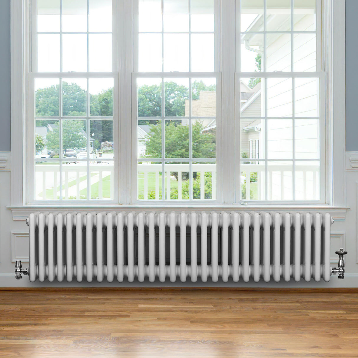 Traditional white 4 column radiator with valves, featuring a sleek design, installed beneath a large window in a bright room