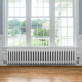 Traditional white 4 column radiator with valves, featuring a sleek design, installed beneath a large window in a bright room