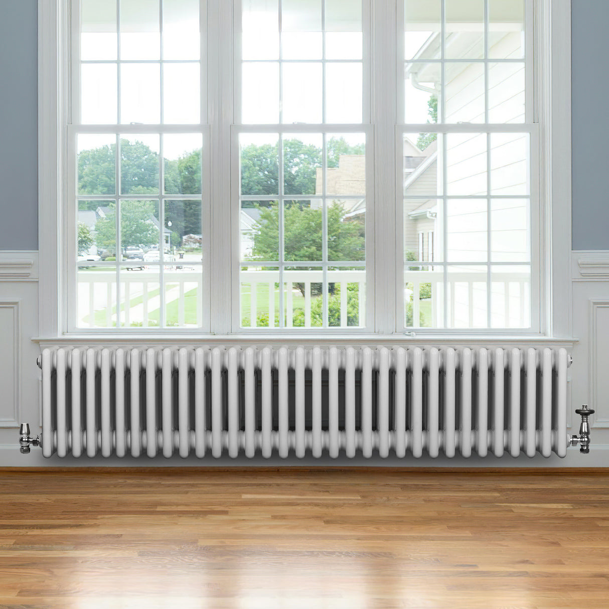 Traditional white 4 column radiator with valves, featuring a sleek design and smooth finish, positioned beneath a large window on wooden flooring