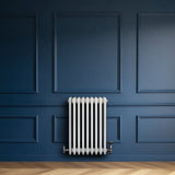Traditional white 4 column radiator with valves, featuring a sleek design against a deep blue wall and wooden floor texture